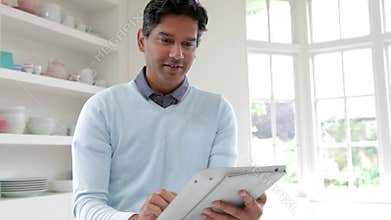 Indian Man Using Digital Tablet In Kitchen At Home
