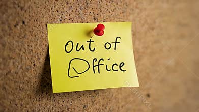 Yellow sticky note with checked checkbox displaying out of office text, secured by red pin onto textured cork board surface