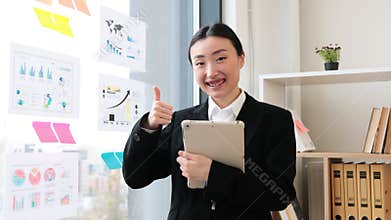 Confident Asian businesswoman giving thumbs up in modern office