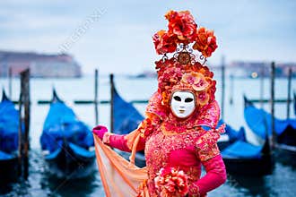 Woman in red dress masked for Venice Carnival in front of typical gondola boats