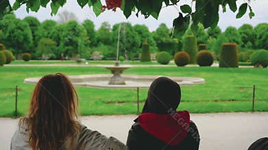 Two people sitting on bench enjoying nature. Happy girls friends chatting.