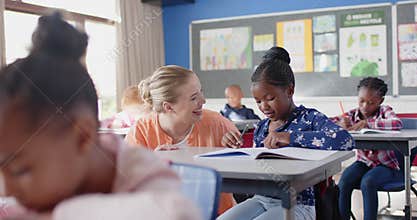 In school, female teacher helping student with writing assignment in classroom