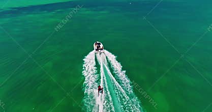 A drone view of a guy skiing behind a speedboat on crystal-clear water. Extreme sports, recreational activities