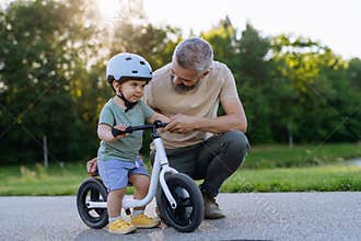 Father teaching toddler son to ride balance bike while wearing safety helmet.