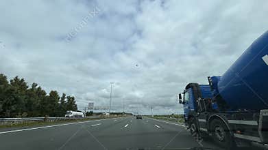 Blue tanker truck driving along multi lane motorway under cloudy sky with