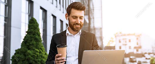Happy Caucasian Man Using Laptop And Drinking Coffee Outdoors In Modern Business District