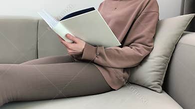 Woman flips book pages while relaxing on sofa at home