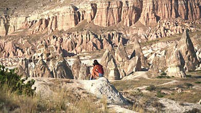 Woman sitting by red sandstone hoodoos in Cappadocia, Turkiye, turkey, travel, valley, fairy chimneys