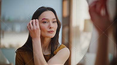 Portrait woman styling eyebrows using brush tool looking mirror with smile.