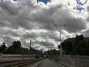 Urban railway corridor beneath dramatic storm clouds with overhead power lines