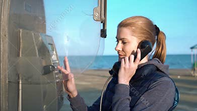 Beautiful attractive young woman talking with friend from telephone booth . Embankment Sunset.