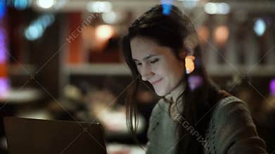 Young happy woman sitting on the cafe and using the laptop. View inside the window on female surfing the Internet.