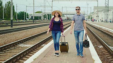 Young happy couple of tourists with travel bags go along the peron along the railroad. Beginning a great journey