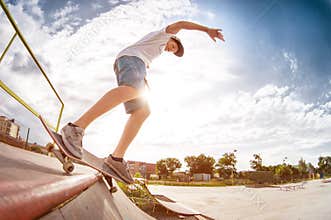 Teenager skater in a cap and shorts on rails on a skateboard in a skate park