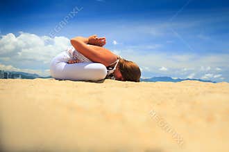 blonde girl sits in yoga asana lotus forward bend on beach