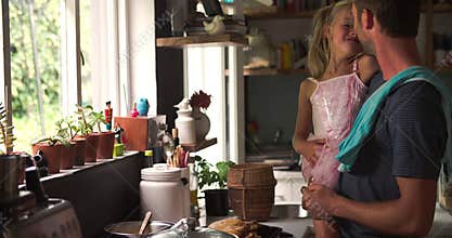Father Cooking Meal Whilst Holding Daughter In Kitchen