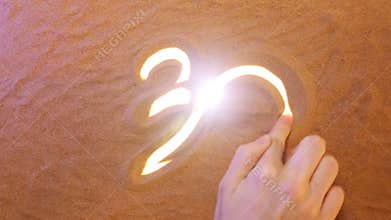 Hand drawing Om Symbol in the sand. Beach background. Top view