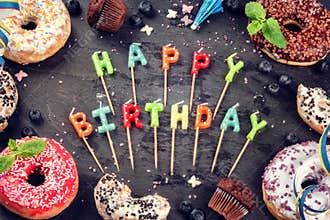 Colorful birthday background with donuts and cupcakes on dark ba
