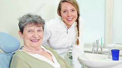 Beautiful smiling dentist and elderly woman giving thumbs up