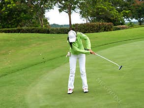 Smiling woman golf player putting successfully ball on green