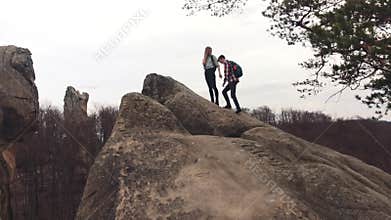 Athletic boy and girl with a tourist backpacks climbing the rocky mountain, then getting on the top, holding their hands