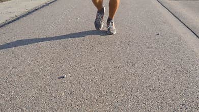 Feet of strong man running on road in summer. Male legs jogging during workout training on country route at sunset