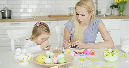 Mother looking at girl coloring eggs