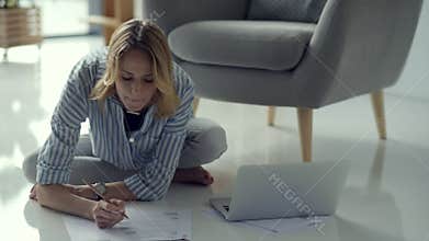 Serious blonde student sitting on floor and doing home task