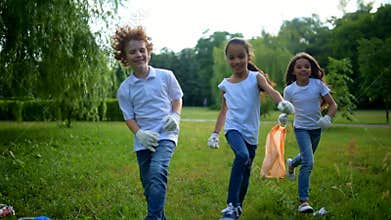 Adorable kids jumping while volunteering and cleaning outdoors