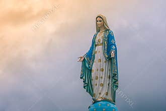 Virgin Mary statue at Catholic church with sunlight in cloudy day background.