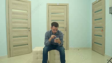 Male patient using phone while waiting for his doctor appointment