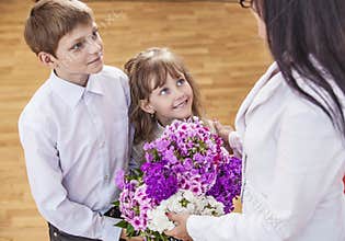 Boy and girl children give flowers as a school teacher in teache