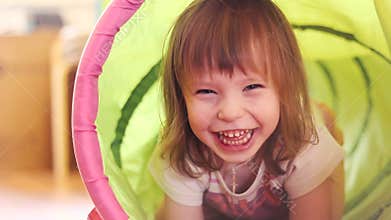 Happy little girl laughing in a children's toy tunnel