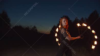 Graceful woman juggling with fire fans at night