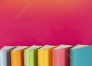 Simple composition of hardback multicolored books, raw of books on pink background. Books stacking with no labels, blank spine