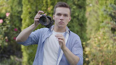 Portrait of young professional male photographer taking photo with camera standing outdoors. Photography, profession
