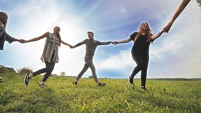 A group of young people lead a round dance holding hands on a summer day. Unity concept.