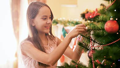 4k footage of beautiful smiling teenage girl hanging colorful bauble on Christmas tree at home. Family decorating house