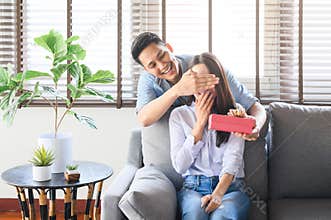 Asian man giving a gift box present to surprise his girlfriend at home