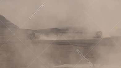Military cargo convoy rides fast in desert sand dunes, leaving behind a massive trail of dust, military operation. The convoy grou