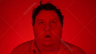 Portrait of stupefied handsome male opens mouth widely, red lighting, Man has shocked expression, being surprised.