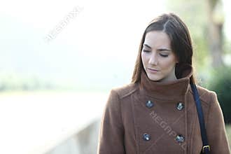 Sad woman walking alone in a park looking down