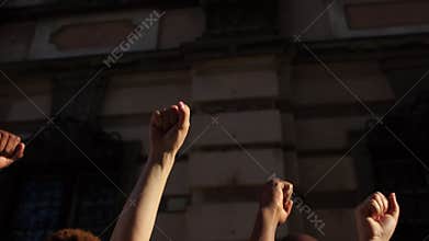 Raised fists against the backdrop of a city wall. People are chanting slogans. The protest against racism. Protests in
