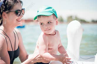 A cute little boy in a blue baseball hat and young attractive mom in sea with an inflatable ring