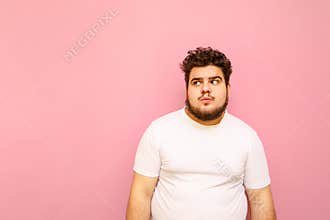 Funny fat man in white T-shirt and curly hair with serious face isolated on pink background, looks away at copy space. Funny