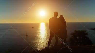 Romantic couple hugs standing on ocean beach edge at sunset