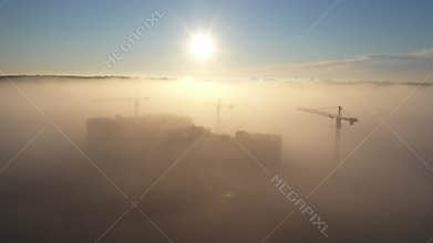 Construction cranes at dawn in the morning mist