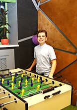 Boy teenager in a blue shirt plays in a table football with figures of football players of both teams in a wooden box in the