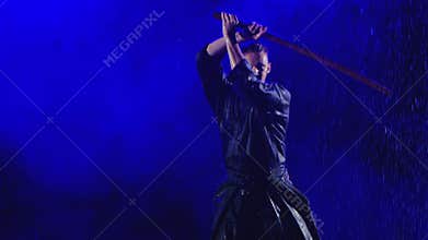 Exercise with a wooden sword of a kendo master in a blue kimono under streams of rain. Shot in slow motion on a smoky