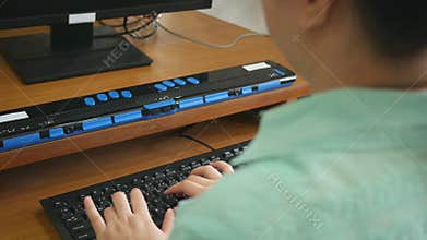 Rear view of blind person woman using computer keyboard and braille display or braille terminal a technology assistive device for